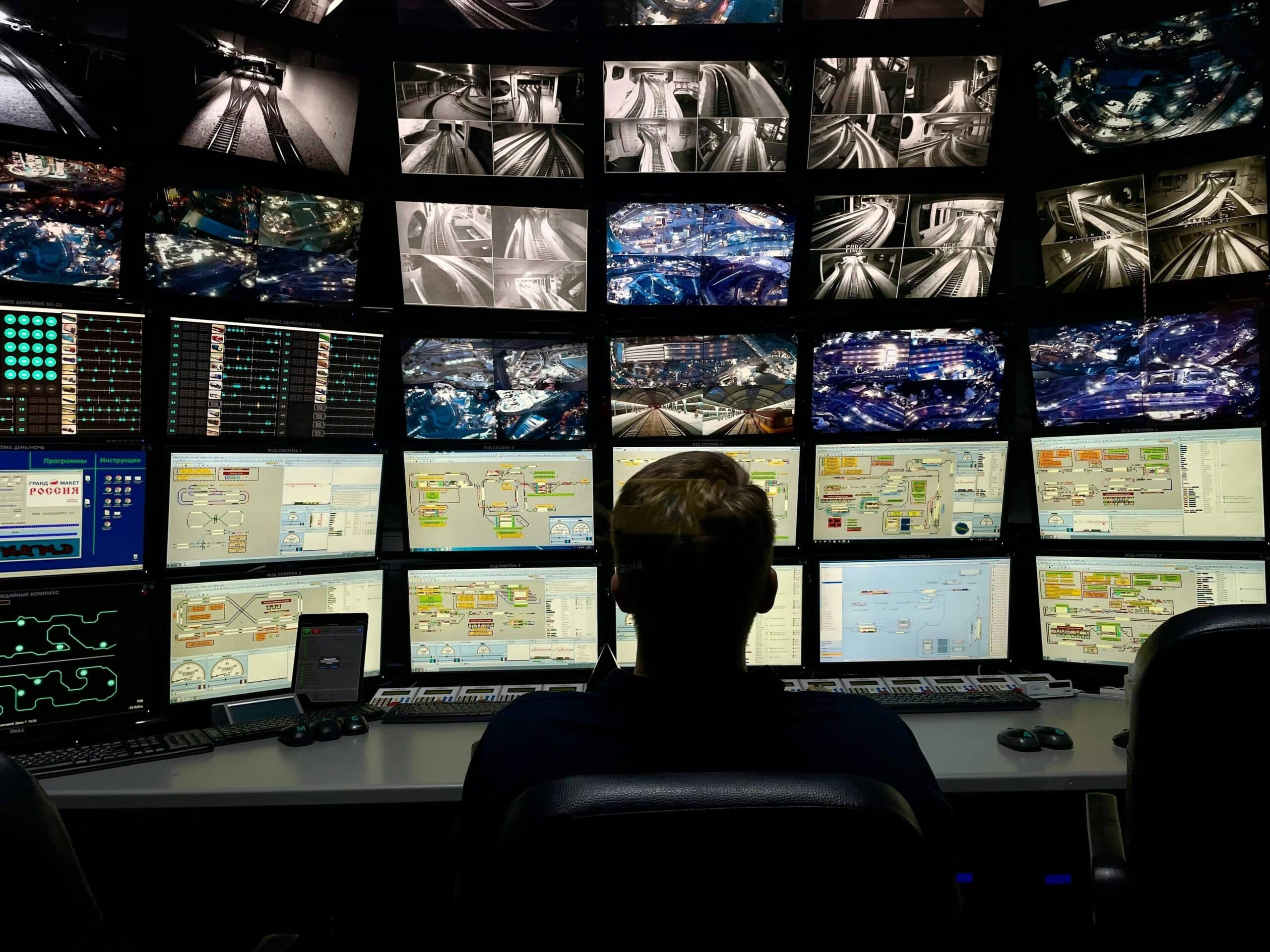 MAN SITTING IN FRONT OF A WALL OF SCREENS