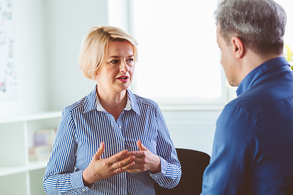 Mature woman gesturing while explaining mental problems to psychotherapist. They are in meeting in psychotherapeutic office.